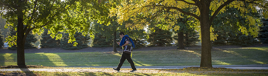 photo of a man with a phone walking on campus