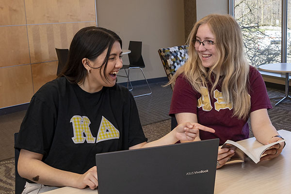 photo of two students in greek tshirts sitting and talking at a table on campus