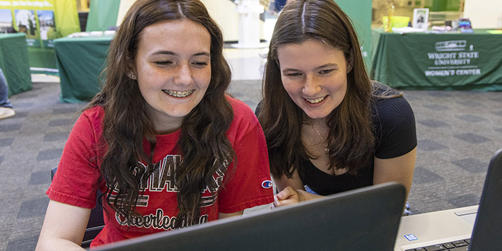 photo of two students smiling and using a laptop