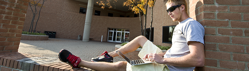 photo of two students sitting outside on campus using a laptop