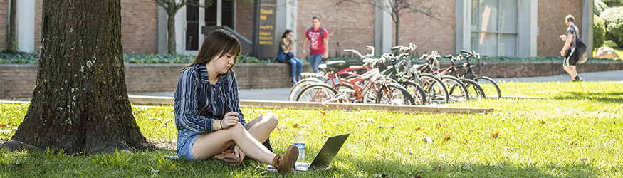 photo of a student with a laptop sitting on the ground on campus