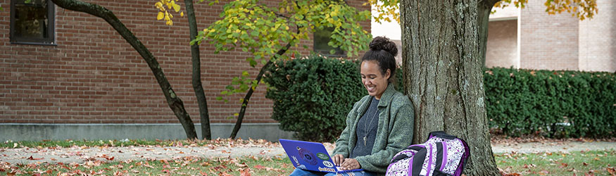 photo of a student sitting by a tree on campus