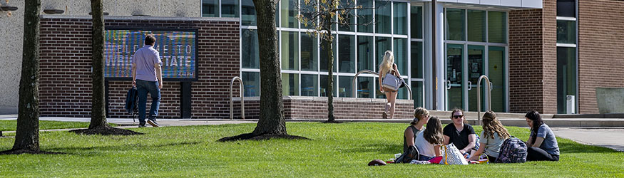photo of students sitting in a circle on the grass outside on campus