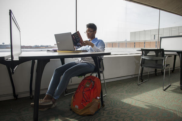 Student sits at laptop, with book