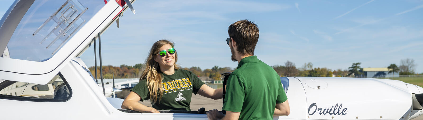 a student and instructor standing next to a plane