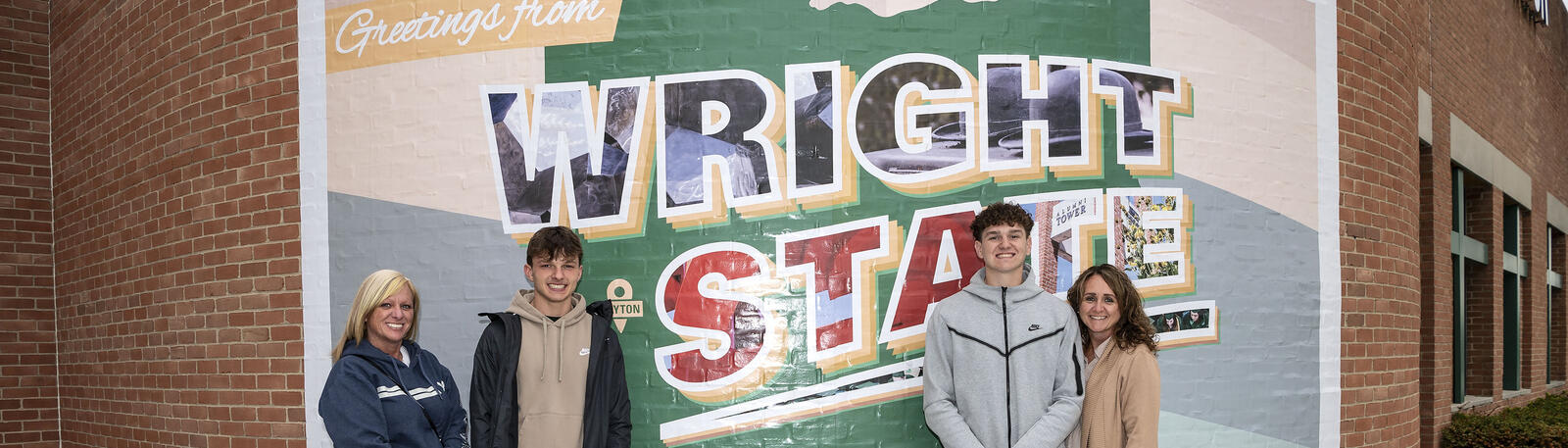 students and parents posing for a photo in front of the Wright State postcard mural