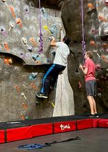 A student starting up an indoor climbing wall with a second student belaying. 