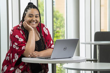 photo of a smiling student sitting at a table with a laptop