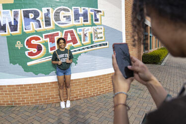 Student having a photo taken standing in front of Wright State wall art