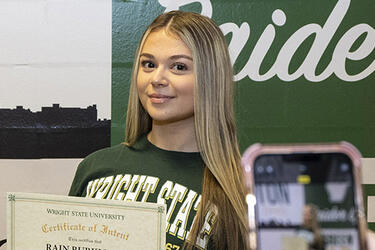 student sitting next to Raider mural