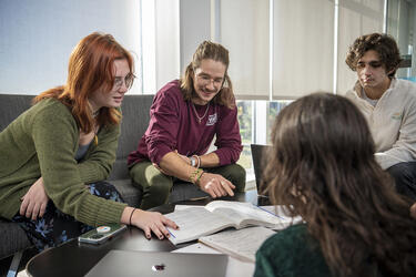 students sitting around a table looking at a book and talking