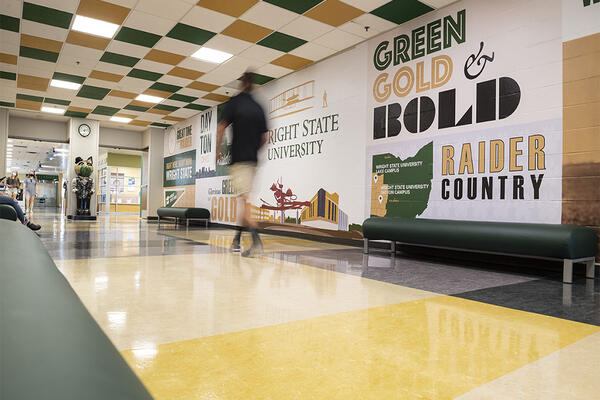 Student walking on campus in front of a mural